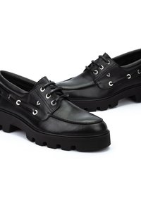 Chaussures en cuir noir avec une semelle en caoutchouc robuste, dotées de lacets, d'œillets métalliques et d'un design mocassin. Texture lisse et bout arrondi.