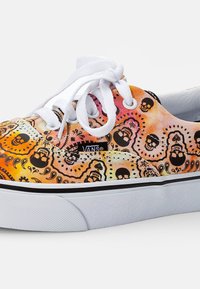 Vans sneakers med et fargerikt mønster som har oransje og rosa nyanser, svarte hodeskaller, hvite snørebånd og kontrasterende svarte detaljer.