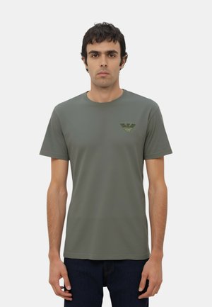 T-shirt in cotone verde oliva con maniche corte, colletto a giro e logo ricamato sul petto. La texture appare liscia e morbida.