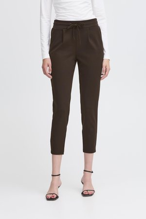 Brown, tapered pants with a drawstring waistband, featuring front pockets and a smooth texture. Paired with black strappy sandals.