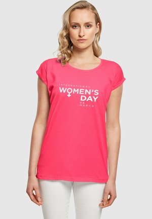 Tricou roz cu mânecă scurtă și decolteu rotund. Text alb care spune "Ziua Internațională a Femeii 08 MARTIE", având simbolul feminin.