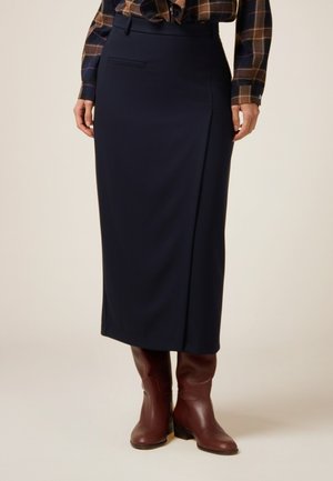 Marineblaue Midi-Rock aus glattem Stoff, mit einem Seitenschlitz, vordere Tasche und strukturiertem Bund. Kombiniert mit braunen Stiefeletten.