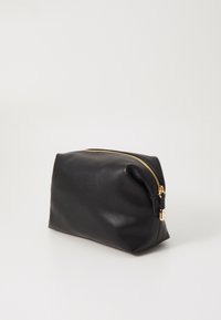 Borsa cosmetica in pelle nera con una cerniera dorata, texture morbida e forma rettangolare. Chiusura con una leggera piega nella parte superiore.