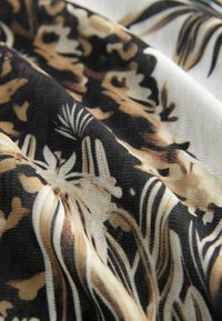 Tissu à motifs contenant un mélange de couleurs noir, crème et beige avec des motifs floraux et de feuillage. Le tissu a une apparence texturée.