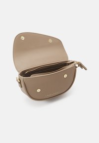 Borsa a tracolla in pelle beige con forma curva, hardware dorato, logo frontale e compartimento interno con zipper. Presenta una chiusura a scatto.