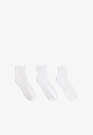 Drie paar eenvoudige witte enkelsokken met geribbelde boordjes, naast elkaar gelegd op een witte achtergrond.