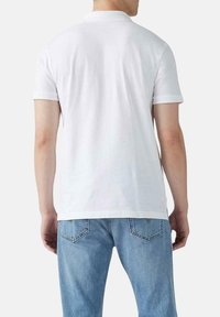 Camisa polo blanca de manga corta con cuello clásico, mostrada desde la parte de atrás, con un corte recto y hecha de suave algodón.