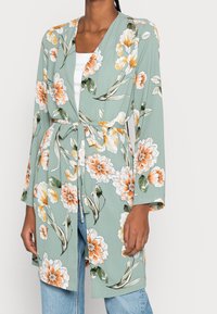 Květinový kimono kabátek ze zelené látky s oranžovými a bílými květinovými vzory, s otevřeným předním dílem, dlouhými rukávy a zavazováním v pase.