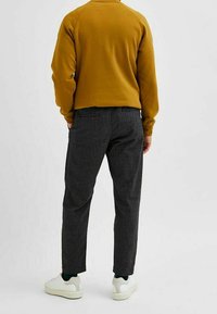 Žlutá mikina s raglánovými rukávy, doplněná o šedé texturované kalhoty a bílé tenisky, pohled zezadu.