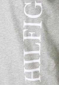 Grå sweatshirt med en stor hvid lodret logo-tekst. Stoffet ser blødt og tekstureret ud med et afslappet design og løs pasform.