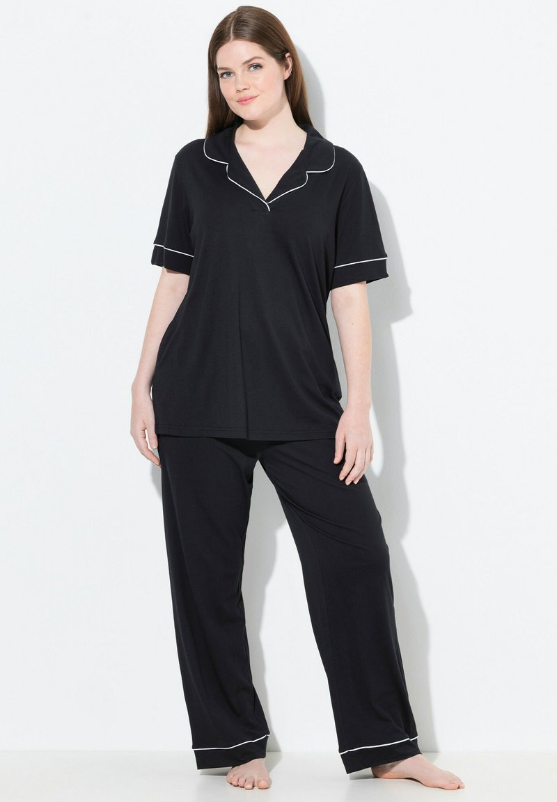 Zwart pyjamapakket met een top met korte mouwen en lange broeken, met witte piping langs de kraag en manchet. Zachte, gladde textuur van de stof.