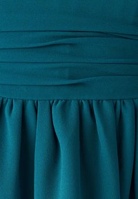 Turquoise jurk van gestructureerde stof, met horizontale plooien op het lijfje en een geplooide rok. Gladde afwerking en vloeiend ontwerp.