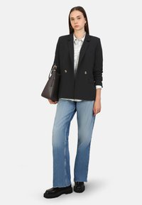 Blazer negro de doble botonadura, camisa de cuadros blanca, vaqueros azul claro, zapatos gruesos negros, sosteniendo un bolso oscuro. Tela suave y diseño ajustado.
