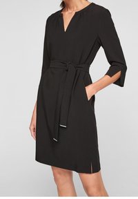 Robe noire avec un décolleté en V, des manches trois-quarts, une ceinture à la taille et des poches latérales. Fabriquée en tissu lisse et léger.