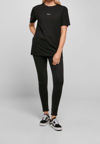 Černé tričko s bílým vyšitým textem, kombinované s černými skinny džíny a černými teniskami s bílými akcenty. Jednoduchý, každodenní outfit.