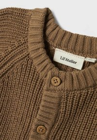 Smeđa pletena svijetla s rebrastim ovratnikom, koja ima gumbiće od materijala koji podsjeća na drvo i oznaku s natpisom "Lil'Atelier."