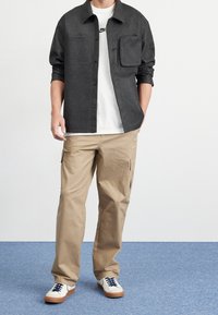 Svart knäppskjorta, vit T-shirt, beige cargobyxor och vita sneakers med marinska snören. Justerbar ficka på skjortan. Strukturert tyg.