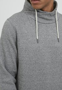 Grijze sweatshirt met een hoge kraag, gemaakt van zachte, textuurrijke stof. Bevat lichte trekkoorden en heeft een relaxte pasvorm.