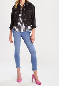 Giubbotto di denim nero, camicia a righe, jeans skinny blu con orlo sfrangiato e tacchi alti rosa. Presenta dettagli con bottoni sui jeans.