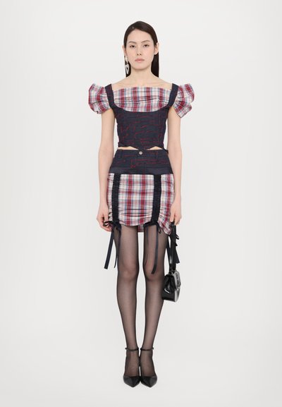Crop top in navy and plaid with puff sleeves, paired with a ruched plaid skirt. Accessories include a small black bag and high heels.