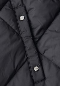 Černá prošívaná vesta s diamantovým vzorem, vybavená stříbrnými druky a hladkou, mírně lesklou texturou.