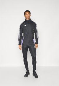 Black athletic ensemble featuring a zippered collar top with white and purple stripes on sleeves, paired with fitted black pants and black shoes.