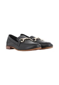 Mocasines de cuero negro con suela plana, que cuentan con un acento de cadena metálica en la parte superior y una suela de goma color beige.