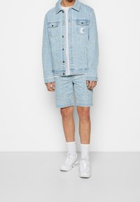 Light blue denim jacket with a textured pattern, paired with matching shorts. White t-shirt underneath, white sneakers, and white socks.