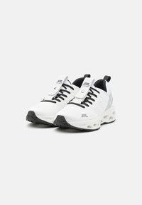 Scarpe atletiche bianche realizzate in rete con un design testurizzato, stringhe nere e una suola spessa e a contrasto. Presentano un logo e una linguetta.