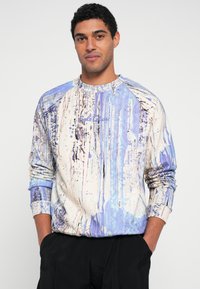 Φούτερ με στρογγυλή λαιμόκοψη σε ανοιχτό μπεζ χρώμα με μπλε και μοβ αφηρημένα σχέδια. Διαθέτει μανίκια ράγκλαν και υφασμάτινη υφή. Ελάχιστη σήμανση.