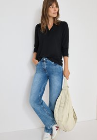 Svart långärmad topp, ljusblå utsvängda jeans, beige axelväska och vita sneakers med röda detaljer. Slät tygkvalitet och avslappnad passform.