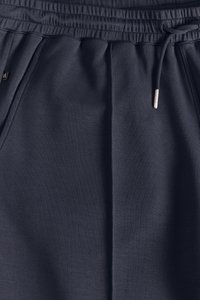 Granatowe spodnie dresowe wykonane z miękkiej, teksturowanej tkaniny, z elastycznym pasem z sznurkiem do regulacji oraz bocznymi kieszeniami zapewniającymi komfort.
