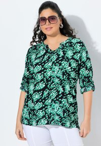 Blusa nera con motivo floreale verde, scollo a V e maniche 3/4 arrotolate fino al gomito. Tessuto leggero con una texture liscia.