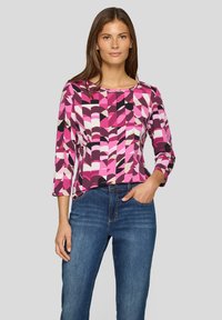 Long-sleeve top with a geometric pattern in pink, black, and beige hues; round neckline; soft fabric; paired with blue jeans.
