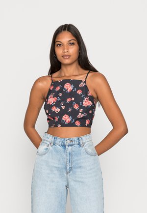 Top floral com alças finas, apresentando um fundo escuro e flores cor-de-rosa/vermelhas. Combinado com jeans de cintura alta de tom azul-claro.