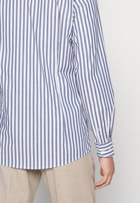 Chemise à rayures bleu et blanc en coton, avec des manches longues, un ourlet arrondi et des poignets avec fermetures à bouton.