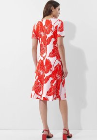 Rotes Blumendruckkleid mit kurzen Ärmeln, A-Linie, knielang, aus glattem Stoff. Kombiniert mit roten Blockabsatzsandalen.