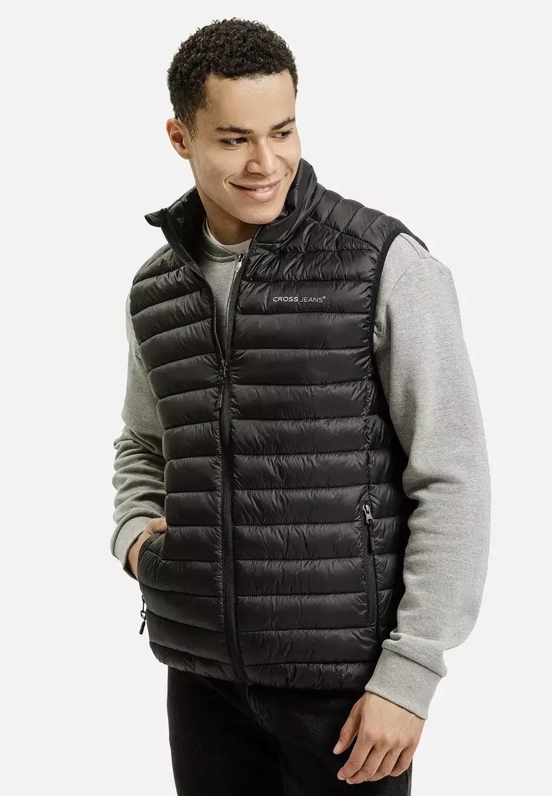 Czarna kamizelka puchowa z pionowym wzorem pikowania, z zamkiem z przodu i bocznymi kieszeniami. Nosi się ją na szaro-sweatshirt, który ma lekką teksturę.