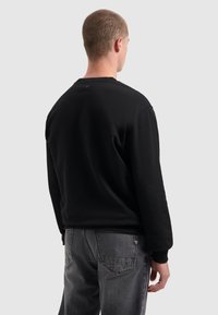 Zwarte sweatshirt, katoenmix, ronde hals, ribgebreide cuffs en zoom. Grijze jeans, relaxte pasvorm, zichtbare naden en zakken, licht versleten afwerking.