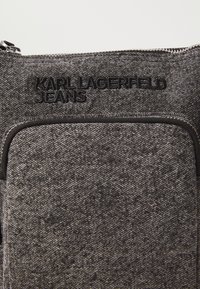 Juodas džinsinis peties krepšys su tekstūruota medžiaga, turintis priekinį užtrauktuką ir iškeltą logotipą "KARL LAGERFELD JEANS".