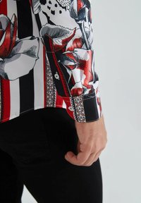 Chemise à manches longues avec un motif floral audacieux présentant des rayures rouges et noires, une finition brillante et une bordure à motif contrasté au niveau du poignet.