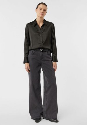 Black satin button-up shirt with long sleeves, paired with wide-leg dark gray jeans featuring a drawstring detail at the waistband.