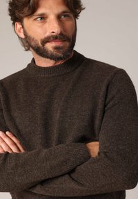 Bruin gebreid sweater met een hoge kraag, voorzien van een gestructureerd oppervlak en geribbelde manchetten. De stof lijkt zacht en warm te zijn.