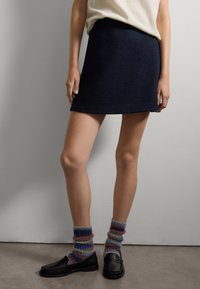 Gonna corta in tessuto blu navy con orlo dritto. Abbinata a mocassini neri e calzini pelosi multicolor, con strisce orizzontali.