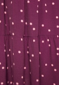 Tissu violet avec de petits pois roses dispersés et des coutures froncées créant une texture et un drapé en étages.