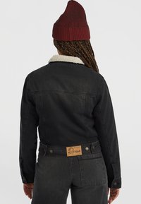 Sort denimjakke med en beige shearlingkrave, tætsiddende design og messingknapper. O'Neill-logo patch på bagsiden af taljen.