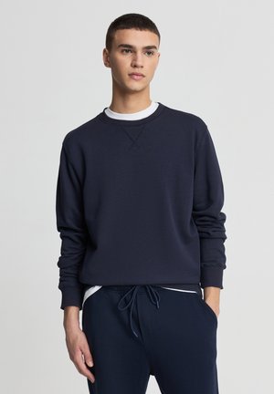 Felpa blu navy in tessuto morbido, con collo rotondo, polsini a coste e vestibilità comoda, indossata sopra una t-shirt bianca.