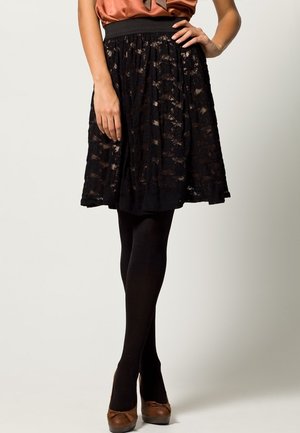 Gonna nera in pizzo con design plissettato, vita elastica, abbinata a collant neri e tacchi alti marroni. Top in satin liscio color ruggine.