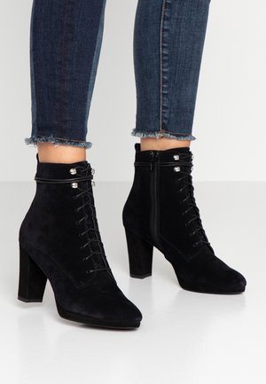 Musta mokkanahkasaappaat, joissa on korkea lohkoheel, nauhakiinnitys edessä ja sivuvetoketju, tumman farkkukankaan päällä, jossa on purjeet.