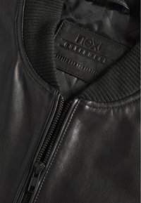 Giubbotto bomber in pelle nera con colletto a costine, dotato di una cerniera full zip e di una fodera trapuntata. Etichetta visibile con "next outerwear."